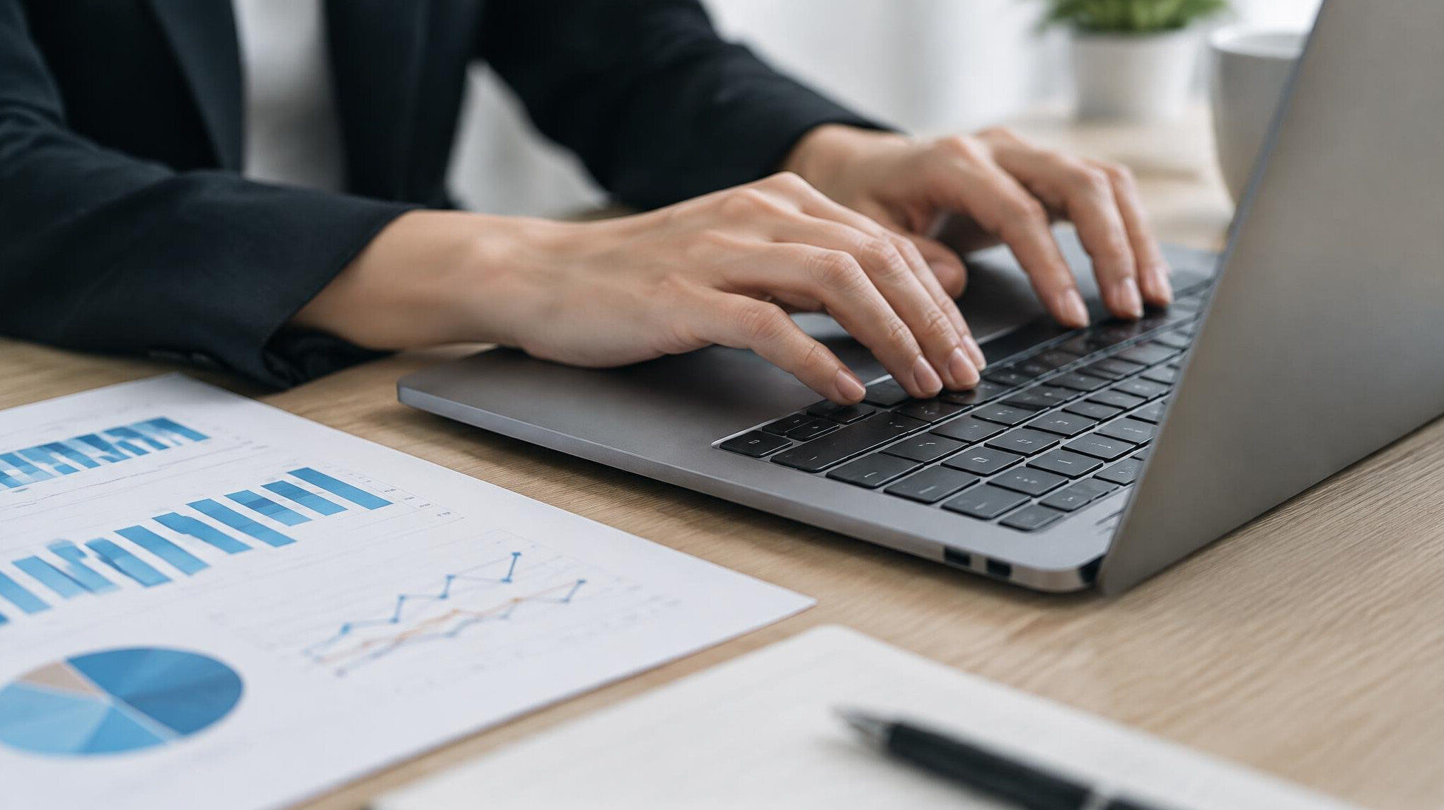 Close-up of hands typing on a laptop next to printed charts